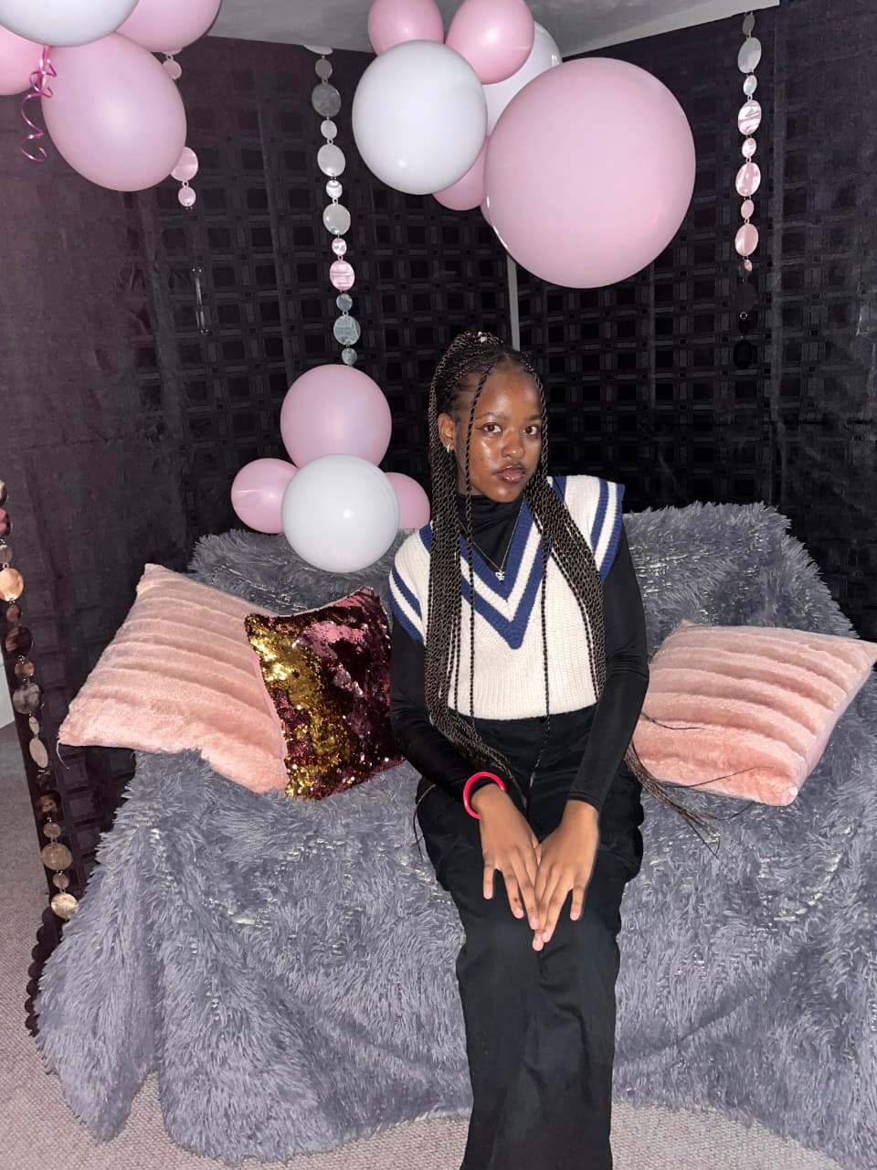 Beauty portrait with braided hair, seated in front of a pink and white balloon backdrop.