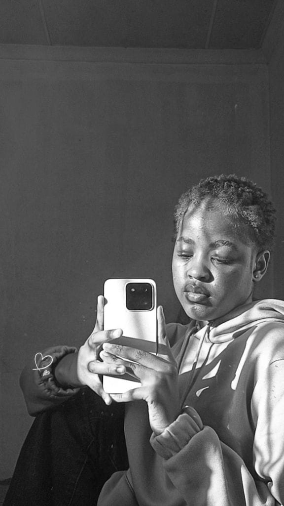 Black and white mirror portrait in a hoodie, head tilted, looking down at the phone screen.