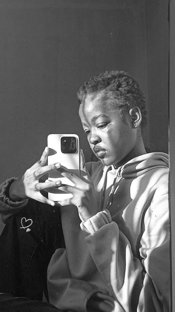 Black and white mirror portrait in a hoodie, closer crop, looking down at the phone screen.