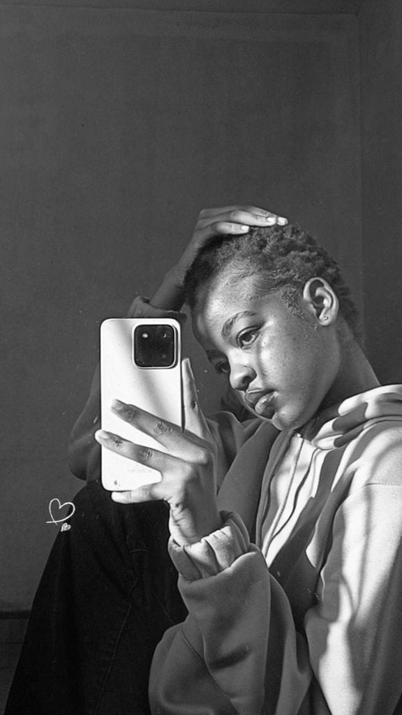 Black and white mirror portrait in a hoodie, hand resting on top of head, looking down at the phone screen.