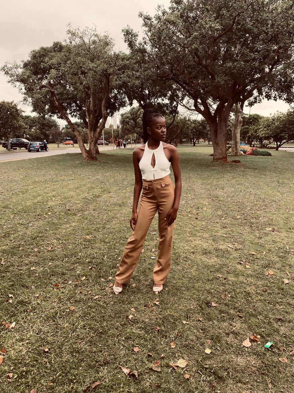 Fashion look: white cutout halter top and camel trousers, full-length in a city park.
