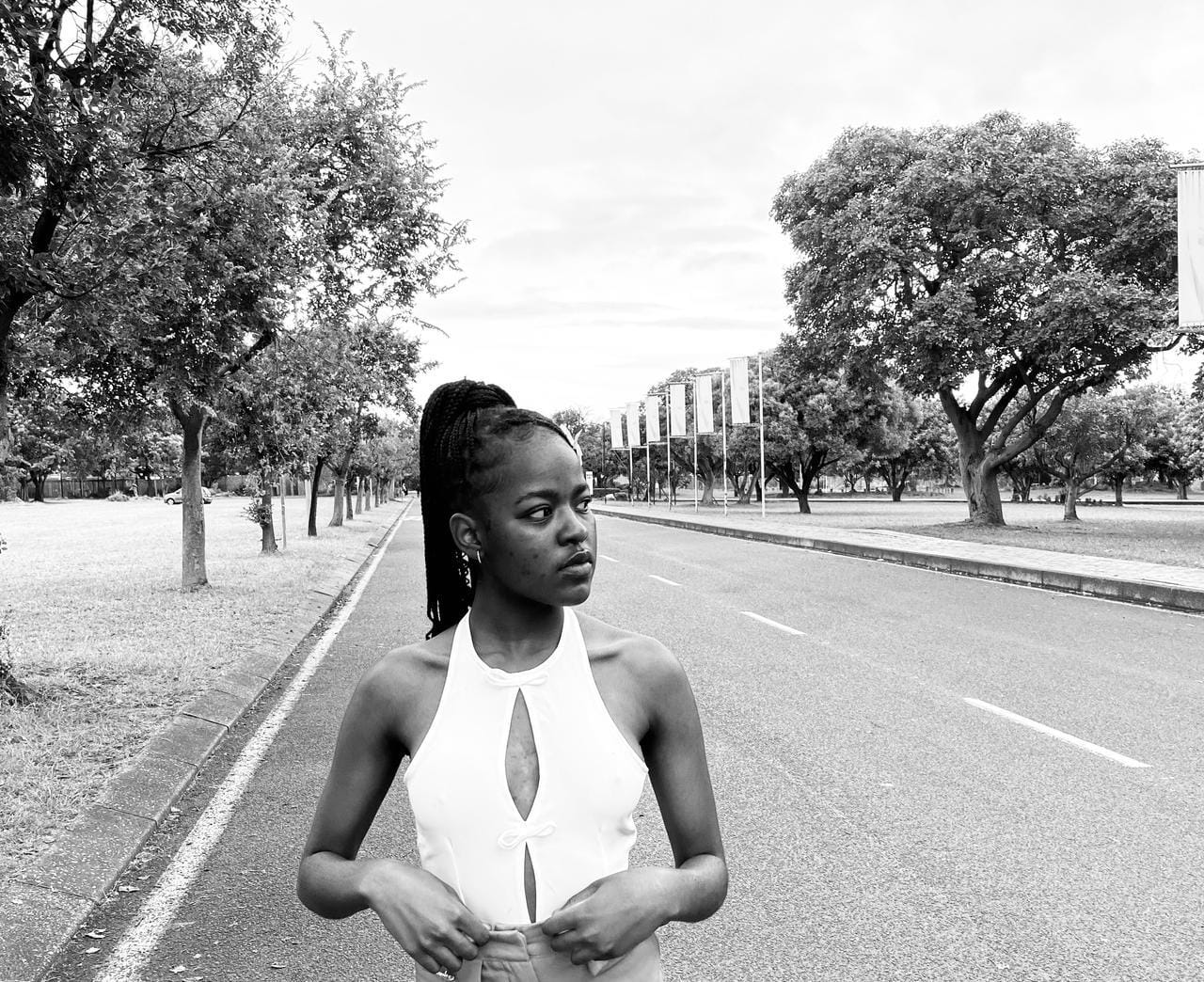 Black and white fashion portrait facing the camera on a tree-lined avenue.