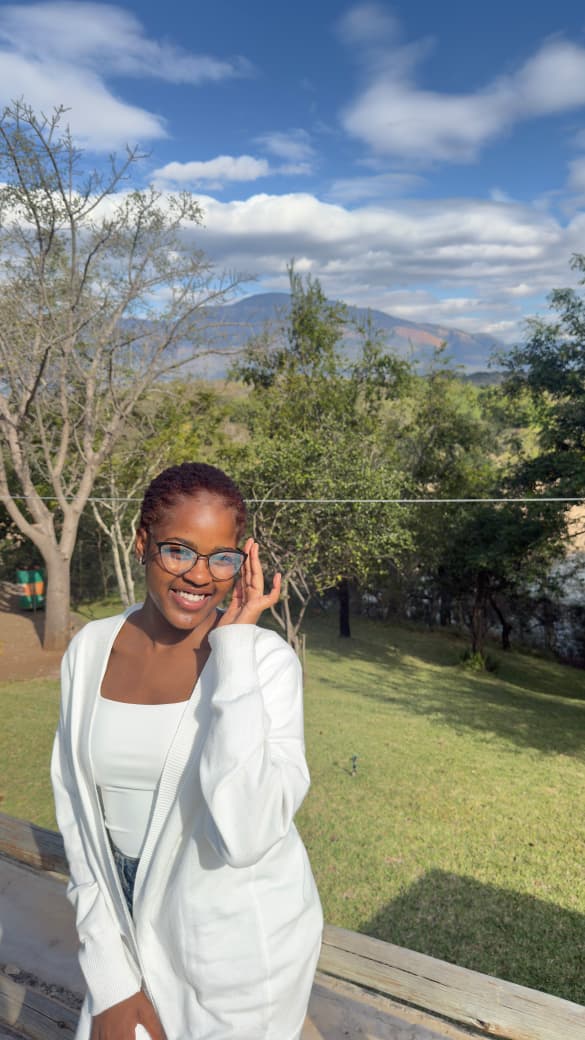 Lifestyle portrait smiling in a white cardigan, garden setting with mountains behind.