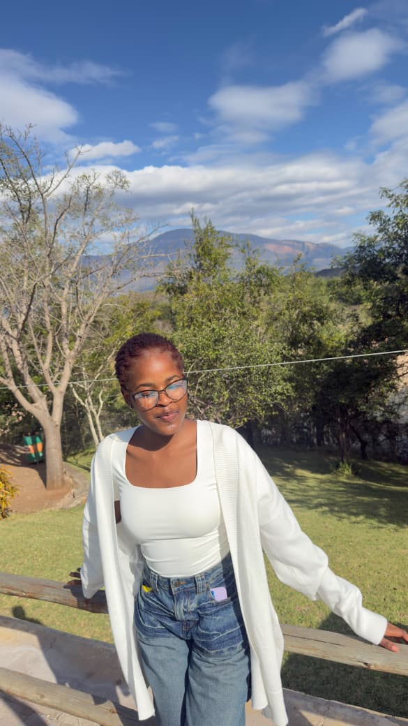 Lifestyle portrait in a white cardigan and jeans, garden setting with mountains behind.
