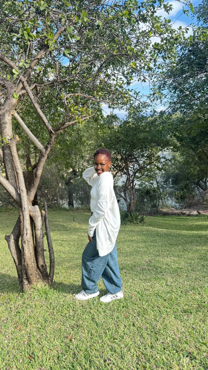 Candid lifestyle portrait laughing over the shoulder, oversized white top and jeans, garden setting.